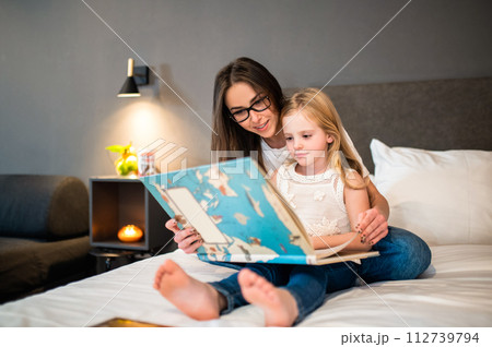 Happy woman with little daughter reading fairy tale in hotel room 112739794