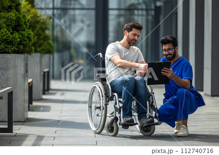 Man sitting in a wheelchair and discussing something with male nurse 112740716