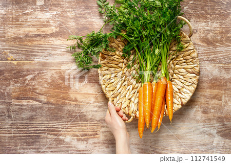 Fresh organic farmer carrots bunch with green tops in a basket on wooden rustic kitchen table, top down view Fresh organic farmer carrots bunch with green tops in a basket on wooden rustic kitchen table, top down view 112741549