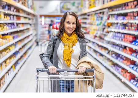 Young woman doing grocery shopping at the supermarket, she is pushing a shopping cart Young woman doing grocery shopping at the supermarket, she is pushing a shopping cart 112744357