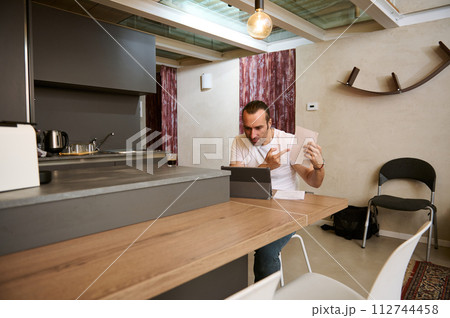 Male freelancer arguing during video conference, showing paper documents to his interlocutors during online meeting 112744458