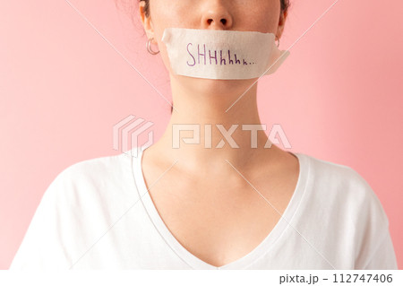 Close up of caucasian woman's face with her mouth taped shut. Tape has the inscription Shhh. Pink background. The concept of women's secrets and problems Close up of caucasian woman's face with her mouth taped shut. Tape has the inscription Shhh. Pink background. The concept of women's secrets and problems 112747406