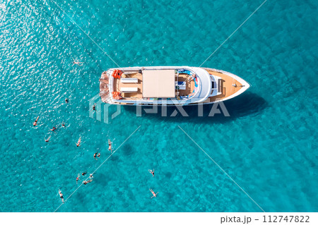 Close-up overhead view of a yacht anchored in the turquoise sea and swimming tourists 112747822