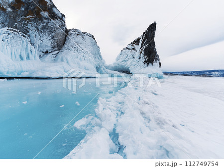 Beautiful winter landscape with blue ice cave grotto and frozen clear icicles. Lake Baikal, Russia. Natural winter background. Great backdrop for your design with copy space. 112749754