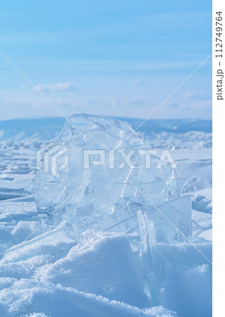 Ice hummocks against blue sky and mountains on Baikal Lake. Transparent blue ice floe. Natural background. Great backdrop for your design with copy space. 112749764