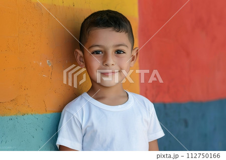 Hispanic child boy 4-6 years old in a white T-shirt without a pattern against the background of a colored wall 112750166