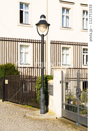 House in residential area with fence, lamp post, and plant in front 112751038