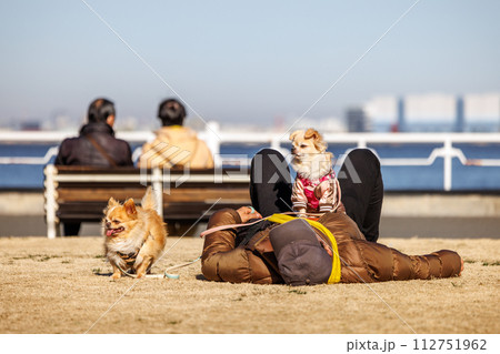 冬の暖かい日に公園の芝生の上で昼寝をする人と愛犬 冬の暖かい日に公園の芝生の上で昼寝をする人と愛犬 112751962