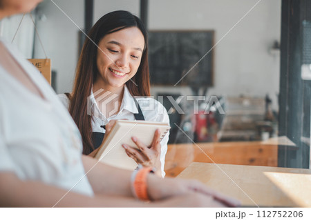 Attentive cafe worker taking a customer order, showcasing excellent service with a personal touch in a modern coffee shop. Attentive cafe worker taking a customer order, showcasing excellent service with a personal touch in a modern coffee shop. 112752206