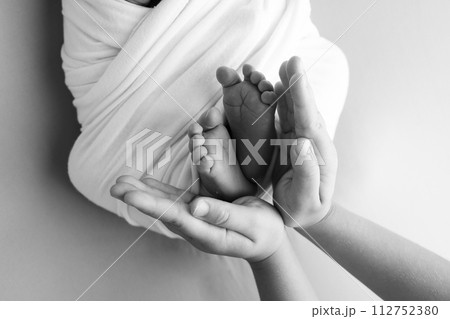 The palms of the father, the mother are holding the foot of the newborn baby. Feet of the newborn on the palms of the parents. Studio macro black and white photo of a child's toes, heels and feet. 112752380