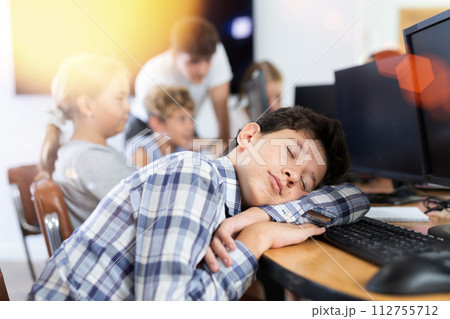 Tired preteen boy sleeping at computer table in training room Tired preteen boy sleeping at computer table in training room 112755712
