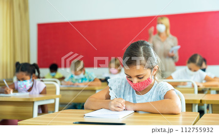Preteen schoolgirl in protective mask studying in classroom Preteen schoolgirl in protective mask studying in classroom 112755932