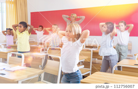 Preteen pupils doing warm-up in class with teacher at lesson 112756007