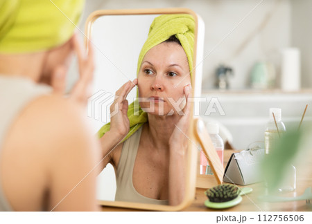 Middle-aged woman examining her facial skin looking in the mirror put on the table 112756506