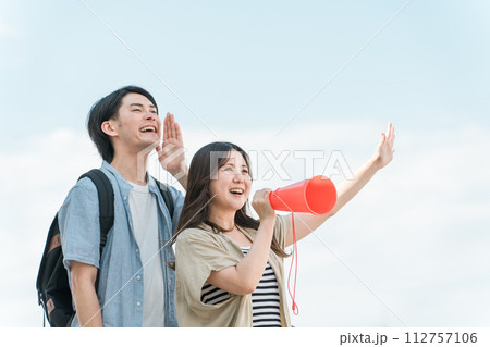 青空の下でメガホンで応援・声援・エールを送る若いアジア人の男女 青空の下でメガホンで応援・声援・エールを送る若いアジア人の男女 112757106