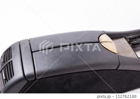 Plastic element of car interior is covered in black leather - armrest or a glove compartment - spare part with air conditioning holes on a white background. Catalog for site. 112762180