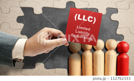 Business hand holding a note with LLC text, the acronym of Limited Liability Company with a row of wooden peg dolls 112762333