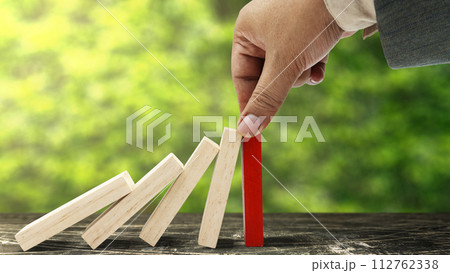 Business hand stopping a falling wooden dominoes 112762338