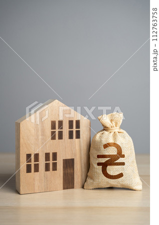Wooden house figure and ukrainian hryvnia money bag. Taxes. Property value appraisal. Make a deal. Buying and selling real estate. Property Insurance. Housing prices. 112763758