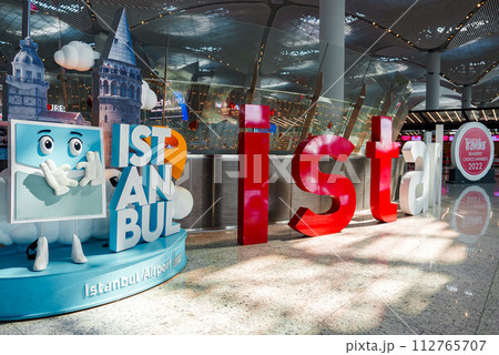 Colorful ISTANBUL letters greet visitors at Istanbul Airport, with a blue suitcase mascot by the Galata Tower. The modern interior shines with natural light, creating a lively, welcoming vibe. 112765707
