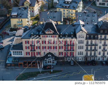 Aerial view of the grand Hotel Bellevue with a red facade in Engelberg, featuring a European alpine design, whitetrimmed windows, and a semicircular canopy entrance. 112765970