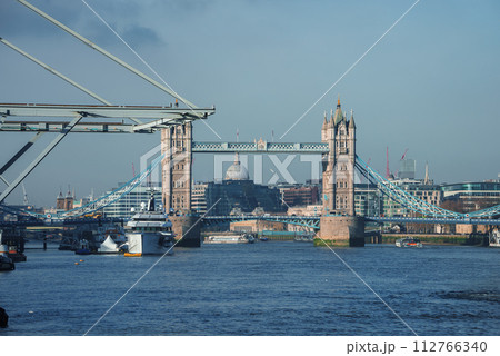 A serene daytime view of London's Tower Bridge with its Gothic architecture and the River Thames below. St. Paul's Cathedral graces the background amidst a clear blue sky. A serene daytime view of London's Tower Bridge with its Gothic architecture and the River Thames below. St. Paul's Cathedral graces the background amidst a clear blue sky. 112766340