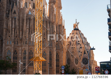 Barcelona's Sagrada Familia, designed by Antoni Gaudi, basks in dawn or dusk light, with intricate facades and a construction crane, hinting at its perpetual incompletion. 112766596