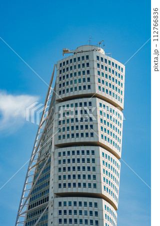 A modern, twisting skyscraper soars into the clear blue sky with wispy clouds in Malmo, Sweden. The Turning Torso's white facade and grid of windows highlight its dynamic, spiraling architecture. A modern, twisting skyscraper soars into the clear blue sky with wispy clouds in Malmo, Sweden. The Turning Torso's white facade and grid of windows highlight its dynamic, spiraling architecture. 112766836