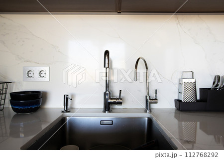 Kitchen brass utensils, chef accessories. Hanging modern kitchen with white marble wall and stone tabletop. 112768292