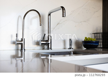 Kitchen brass utensils, chef accessories. Hanging modern kitchen with white marble wall and stone tabletop. 112768293