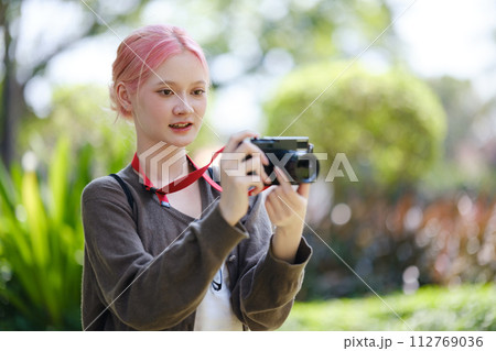 Beautiful Young artist Woman taking photo in flowers garden. Young cute girl carry the camera in the garden. 112769036