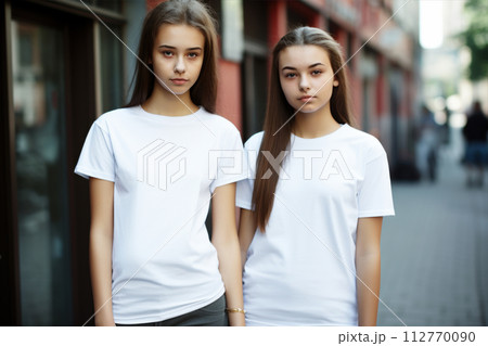 Two girls models wearing plain white t-shirts posing against trees and grass. 112770090