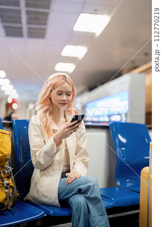 Happy asian tourist woman using mobile smartphone with suitcase traveling between waits for flight in Airport Terminal, flight check in, Tourist journey trip concept Happy asian tourist woman using mobile smartphone with suitcase traveling between waits for flight in Airport Terminal, flight check in, Tourist journey trip concept 112770219