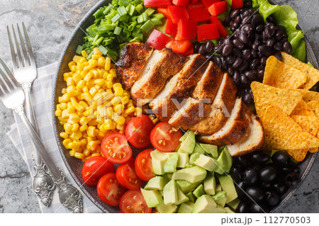 Southwest salad of chicken, corn, peppers, olives, avocado, tomatoes and onions close-up on the plate. Horizontal top view 112770503