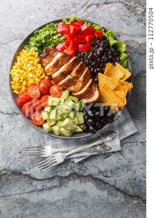 Santa Fe salad combines lettuce, tomatoes, corn, black beans, pepper, avocado, olive and chicken closeup on the plate. Vertical top view 112770504