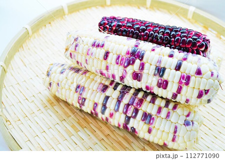 白背景にざるの上に載せられた紫と白のバイカラーのもちとうもろこし 112771090