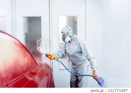 Male worker in grey costume cloth wearing chemical protective mask using spray gun and airbrush and painting a red car. 112771897