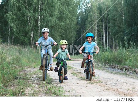 Three happy children ridding bicycles at country dirt road in woods. Three happy children ridding bicycles at country dirt road in woods. 112771920