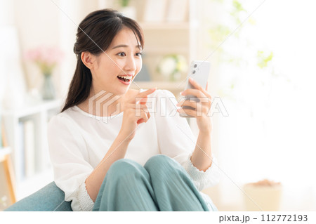 リビングでスマホを見る若い女性 112772193