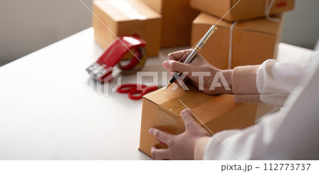 Woman is writing a list of customer on paper before shipping to them, she runs an ecommerce business on websites and social media. Concept of selling products online Woman is writing a list of customer on paper before shipping to them, she runs an ecommerce business on websites and social media. Concept of selling products online 112773737