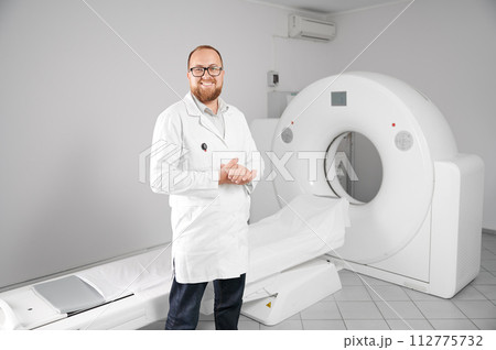 Portrait of smiling doctor with medical computed tomography or MRI scanner. Concept of medicine, healthcare and modern diagnostics. 112775732