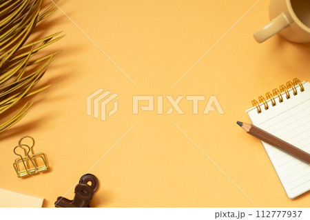 Workspace concept. Note, memo pad, clip, colored pencil, mug cup, plant on orange desk background. flat lay, top view, copy space Workspace concept. Note, memo pad, clip, colored pencil, mug cup, plant on orange desk background. flat lay, top view, copy space 112777937