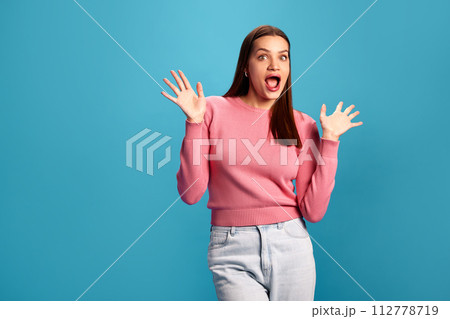 Emotional young woman in pink sweater and jeans expressing positive shock and excitement against blue studio background. Surprise Emotional young woman in pink sweater and jeans expressing positive shock and excitement against blue studio background. Surprise 112778719