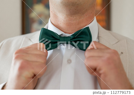 Gentleman adjusts elegant green bow tie, preparing for formal event 112779173