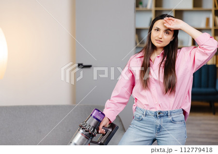Tired and exhausted woman vacuuming house, cleaning rug carpet in living room, frustrated with doing much work about the house resting for a minute wiping forehead after finishing work, taking break. Tired and exhausted woman vacuuming house, cleaning rug carpet in living room, frustrated with doing much work about the house resting for a minute wiping forehead after finishing work, taking break. 112779418