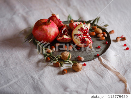 Image of Still Life with Turkish Pomegranate and olive branch on old retro plate. Dark wood background, antique copper plate. Fresh ripe whole pomegranates, opened pomegranate and seeds Image of Still Life with Turkish Pomegranate and olive branch on old retro plate. Dark wood background, antique copper plate. Fresh ripe whole pomegranates, opened pomegranate and seeds 112779429