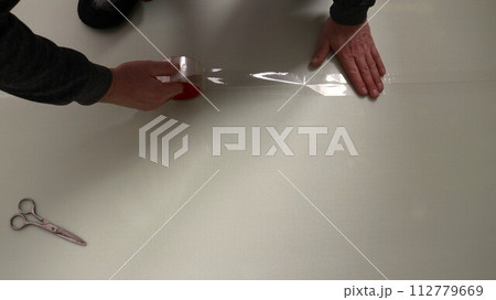 A man sticks a transparent wide tape to the joint of two polyester sheets of insulation for the floor, gluing the edges of a soft substrate under the laminate, do it yourself 112779669