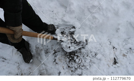 View from the upper angle to clean the large layer of snow with a shovel in the hands of a man in black winter clothes, the removal of snowdrifts in the garden or yard after abundant snowfall 112779670