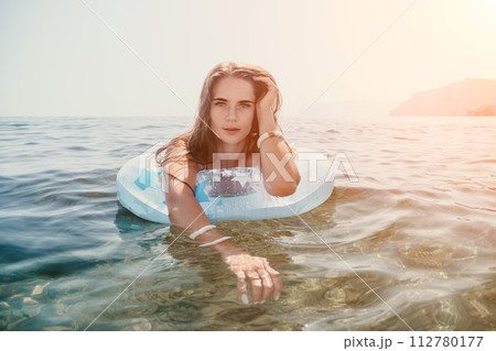 Woman summer sea. Happy woman swimming with inflatable donut on the beach in summer sunny day, surrounded by volcanic mountains. Summer vacation concept. Woman summer sea. Happy woman swimming with inflatable donut on the beach in summer sunny day, surrounded by volcanic mountains. Summer vacation concept. 112780177