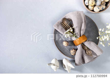 Napkin, vintage cutlery, quail eggs, gray plate, flowers, ceramic bunnies. Gray Easter table setting 112780994